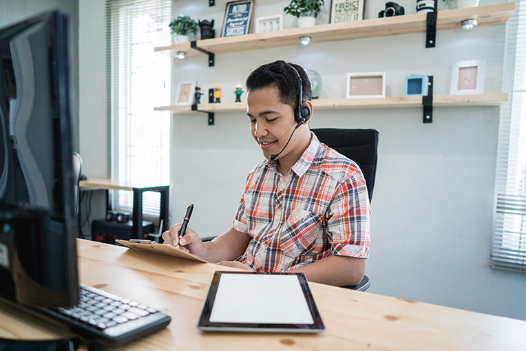 View Program Business Management & Marketing Man with headset on, writing on paper. 